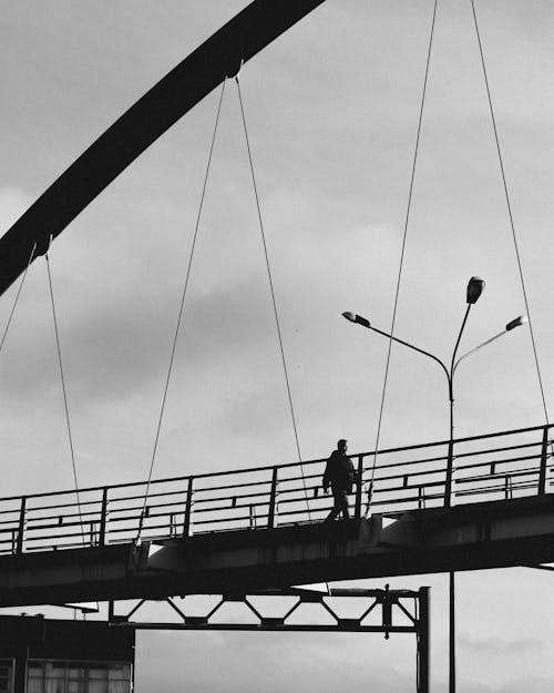 Grayscale Photography of a Man Walking on the Bridge