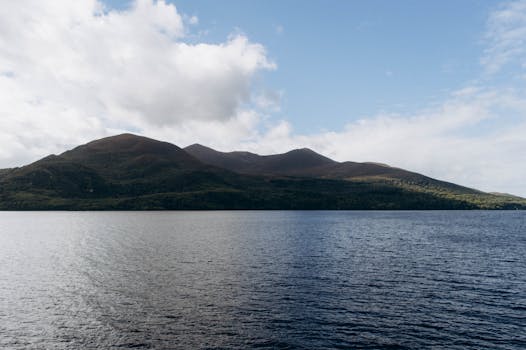 A stunning view of a mountain range with calm sea and cloudy sky.