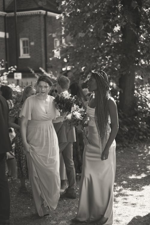 A Grayscale Photo of Women in Long Dresses Standing on the Street