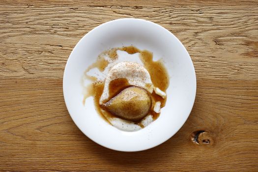 Top view of a poached pear with caramel sauce on a rustic table setting.