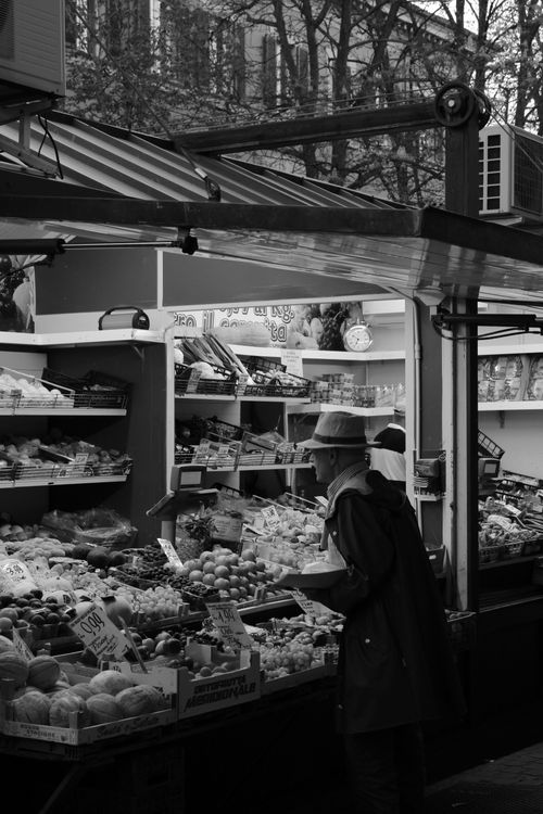 Free Grayscale image of a street market stall in Bologna, Italy, featuring a man shopping for fresh produce. Stock Photo