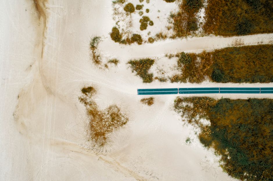 Aerial perspective of a sandy beach featuring a solitary road among dunes and vegetation.