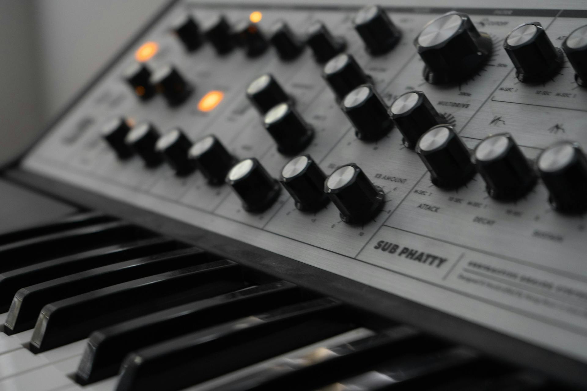 Detailed view of an analog synthesizer's knobs and keyboard with illuminated controls.