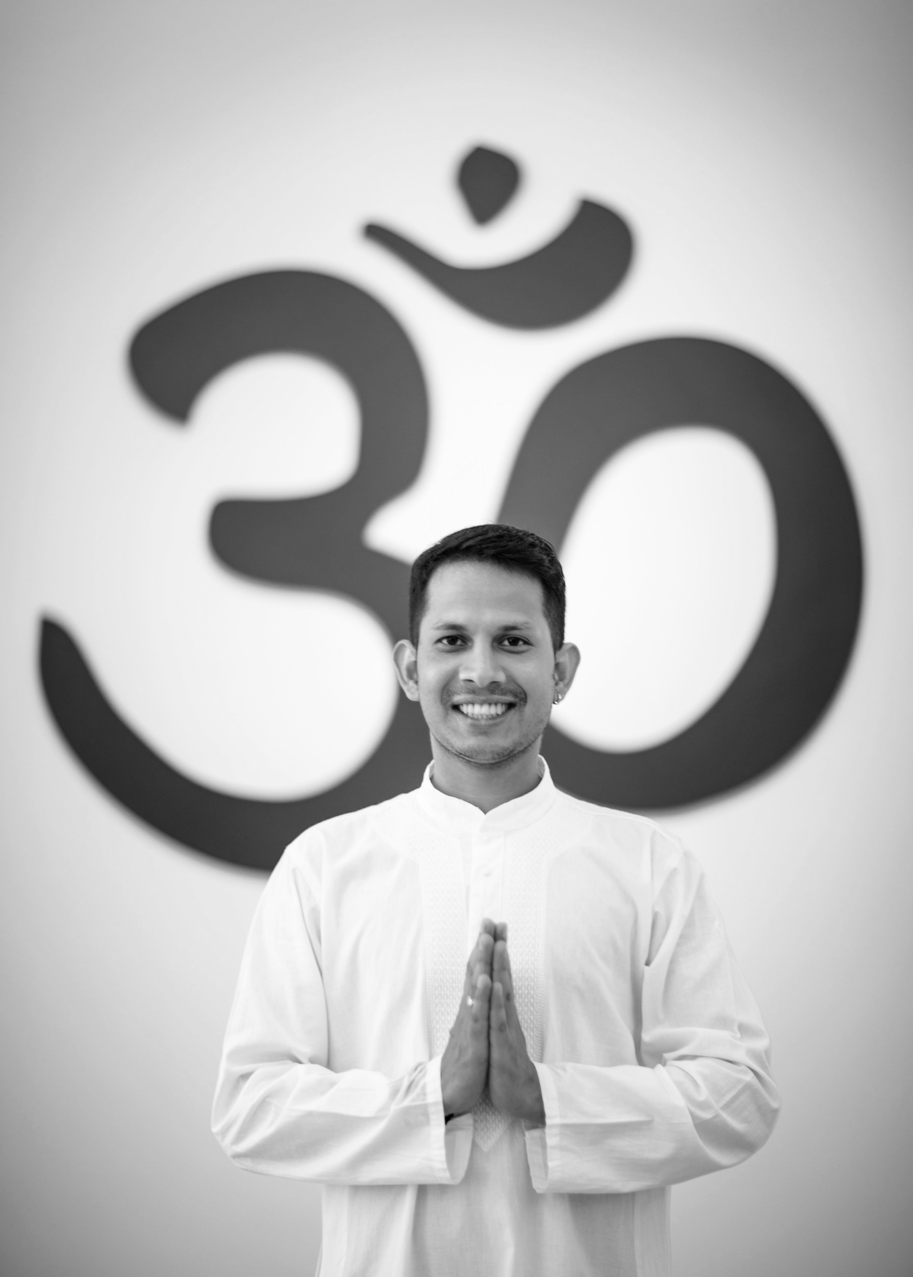 Portrait of a smiling man in traditional attire with Om symbol in background.