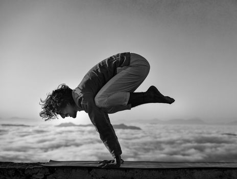 Person performing yoga handstand above clouds in grayscale.