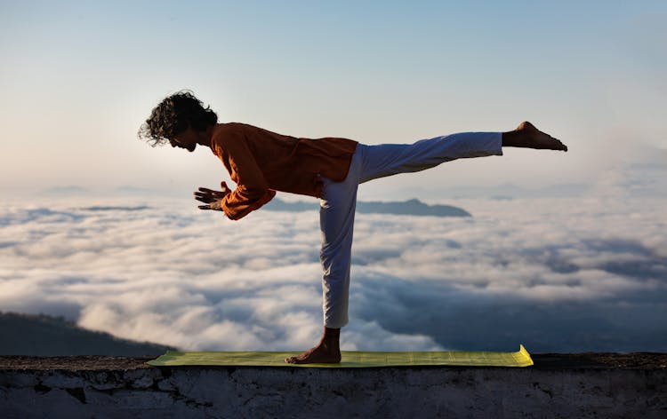 Man Practicing Yoga On Building Edge On Sky Background