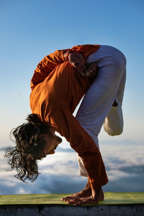 Free Man performing a challenging yoga pose outdoors against a blue sky and clouds. Stock Photo