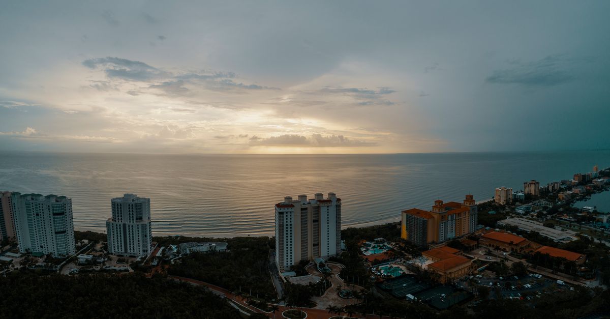 Scenic aerial view of a coastal city with high-rise buildings at sunset, overlooking the ocean.