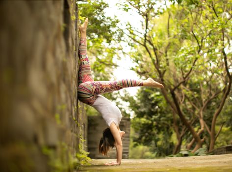 A woman performs a handstand against a wall in a serene outdoor setting, showcasing flexibility and strength.