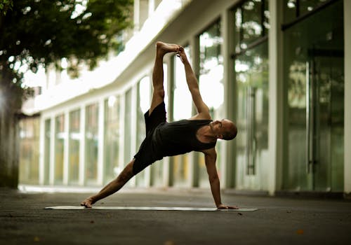 Athletic man performing yoga pose outdoors by modern building. Urban fitness concept.