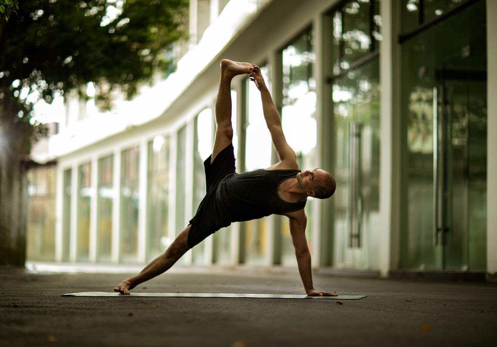 Athletic man performing a yoga pose outdoors near a modern building as part of cross-training