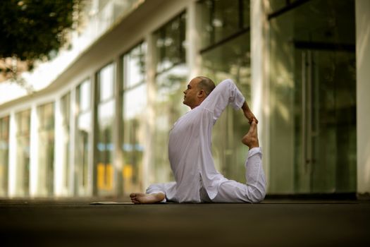 Person practicing yoga outdoors near a modern building, showcasing balance and flexibility.