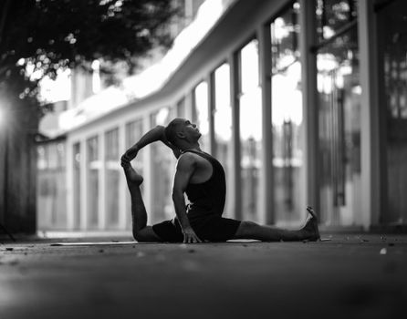 Man performing a yoga stretch outdoors in an urban area, captured in black and white.