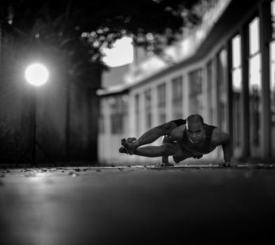 A man performing a complex yoga pose outdoors, captured in dramatic black and white.