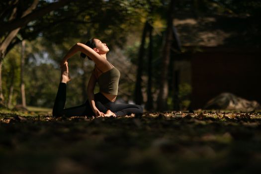 A woman performing a yoga pose in a serene forest environment, showcasing flexibility and balance.