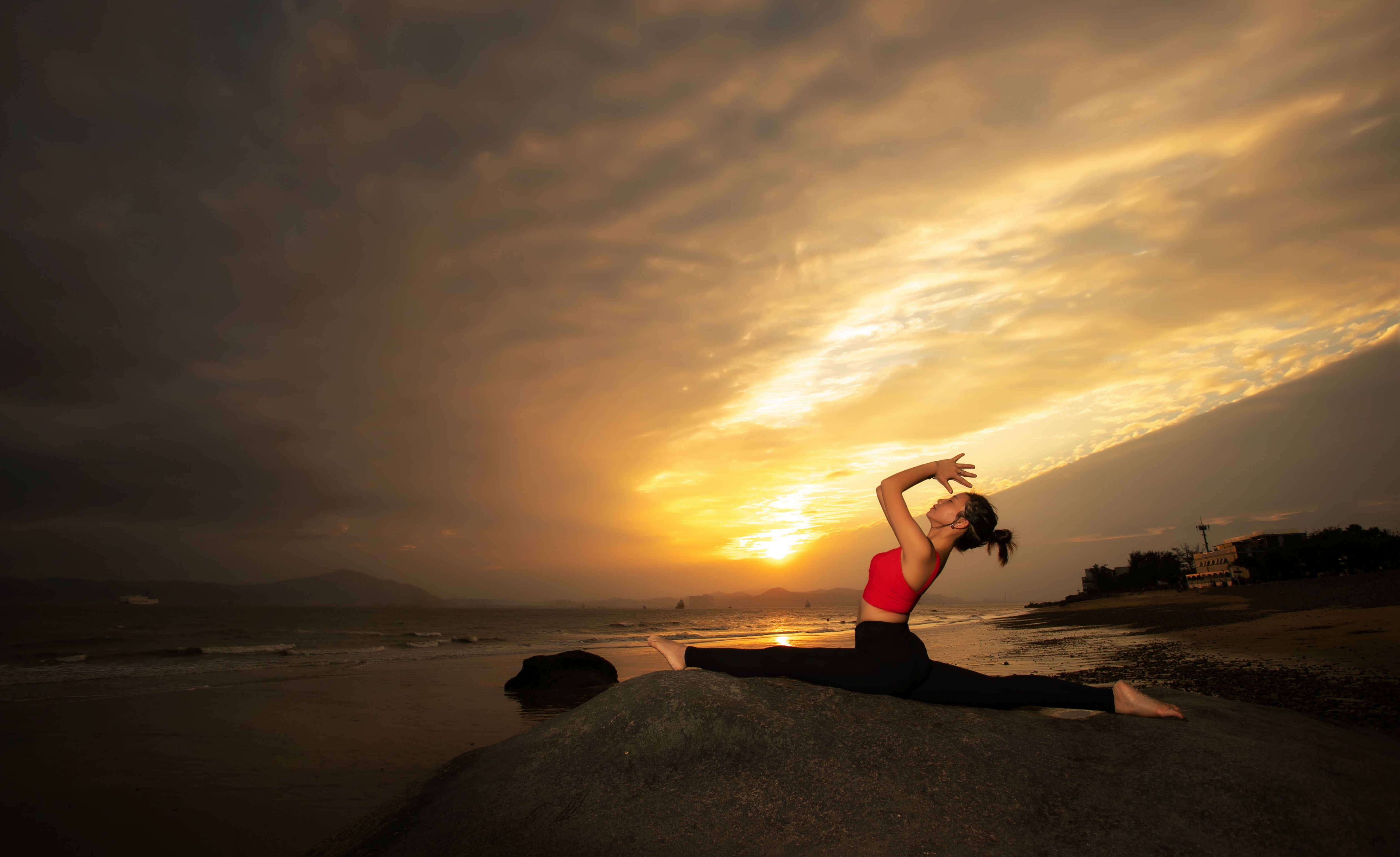 A practitioner stretches on a mat by the water in warm evening light.