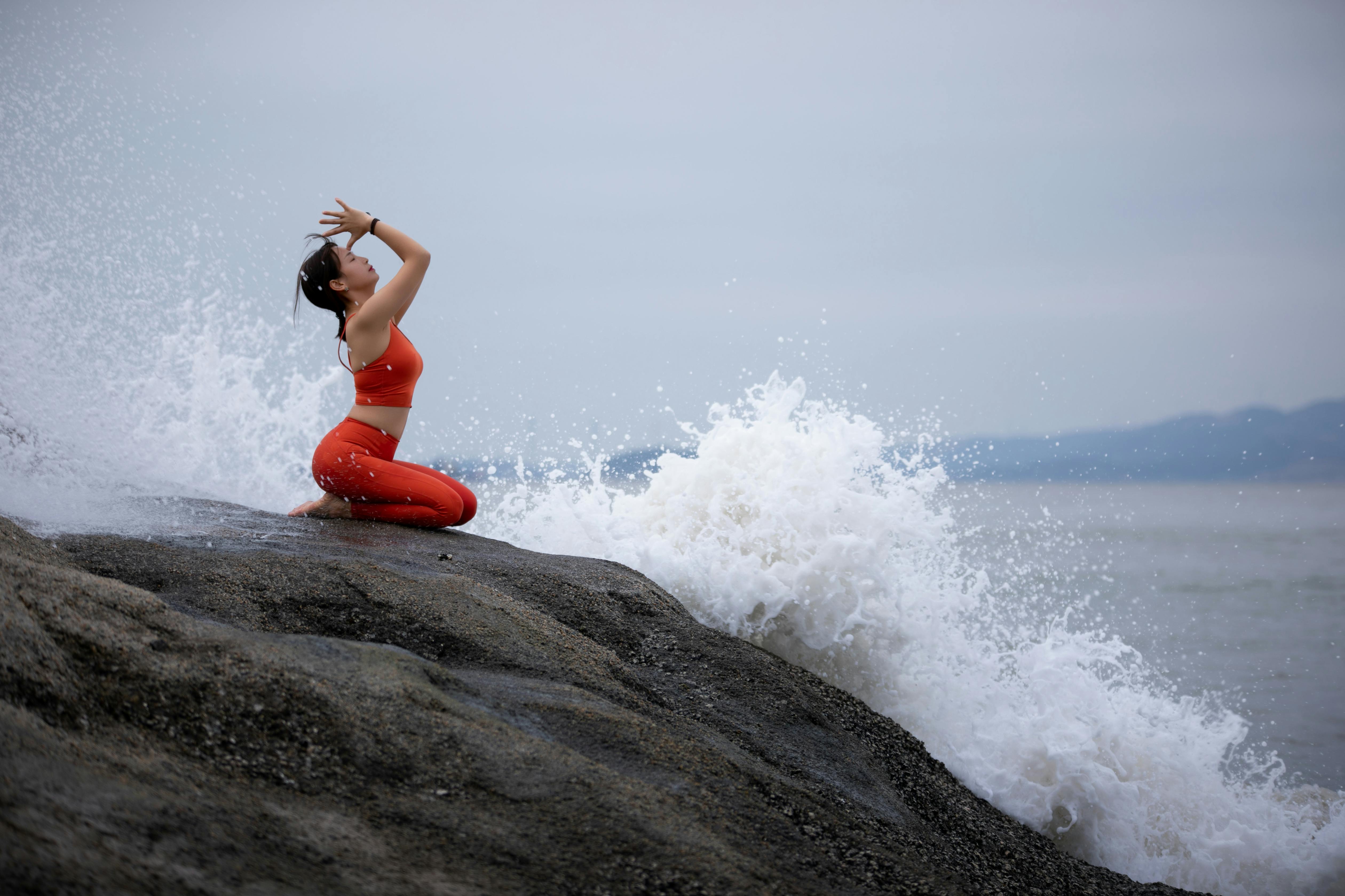 A woman in bright activewear practices yoga by the sea with crashing waves in the background, temsil eden denge ve adaptasyon görseli.