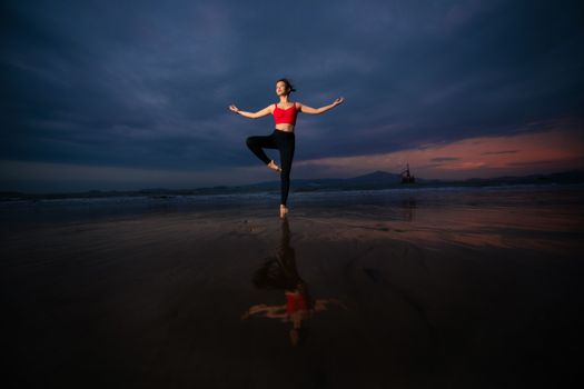 Woman practicing yoga on a beach at sunset, reflecting tranquility and balance.