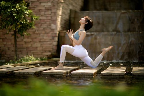 Free Woman performing yoga pose by a serene waterfall and stone path outdoors. Stock Photo
