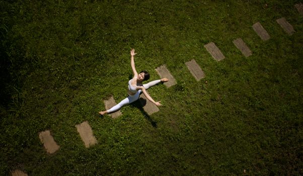 Aerial photo of a woman practicing yoga poses on a grassy lawn, surrounded by nature.