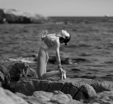 Woman practicing yoga on rocky coastline, grayscale image.