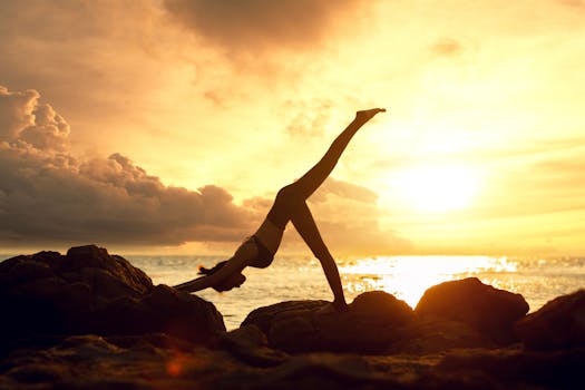 Silhouette of a woman practicing yoga on rocks by the sea during a stunning sunset.