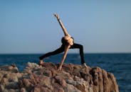 日落时分，一个女人在海边的岩石悬崖上做瑜伽姿势，促进健康和宁静