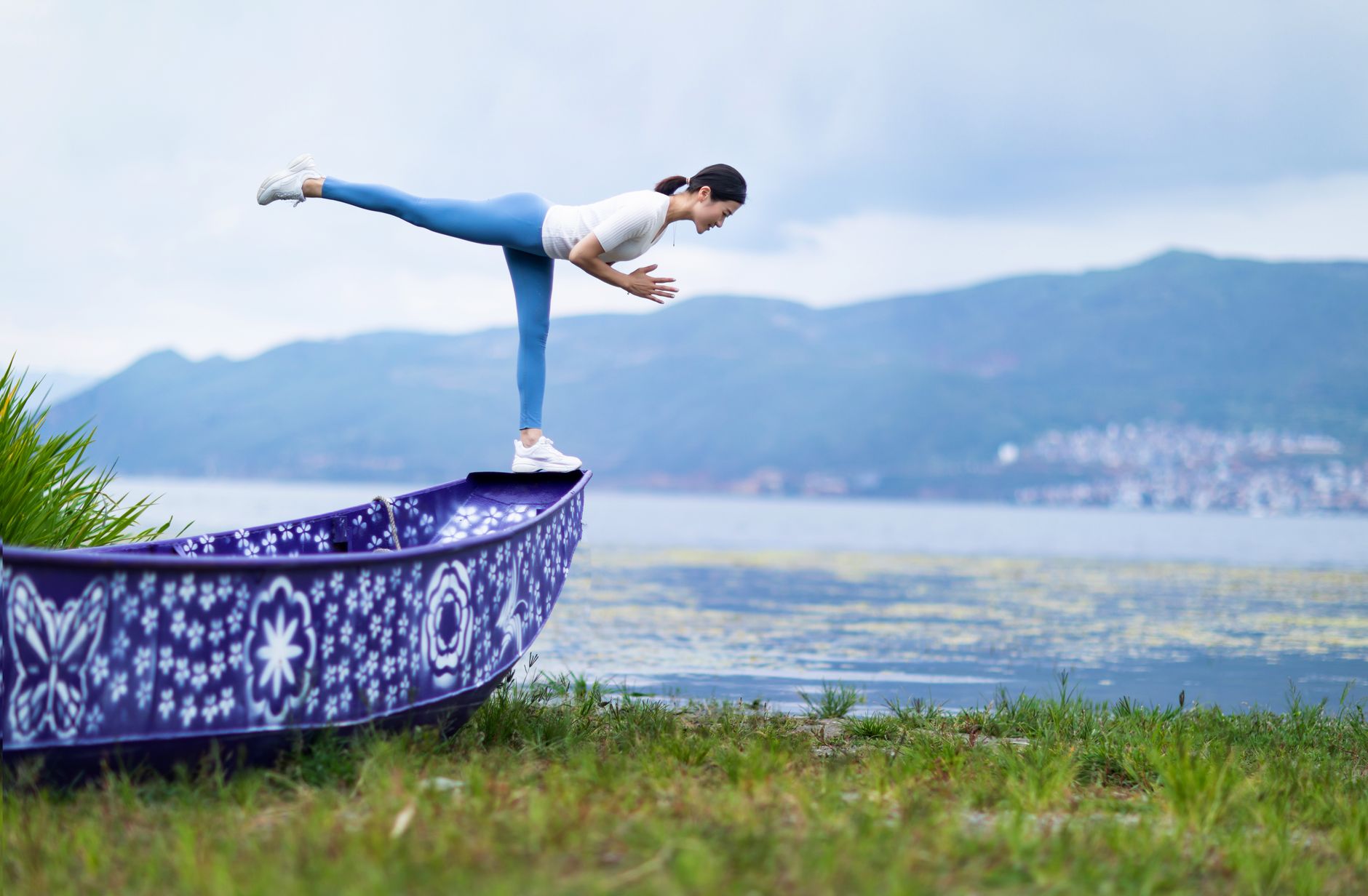 Asian woman practicing yoga pose balancing on a painted boat by the serene coast.