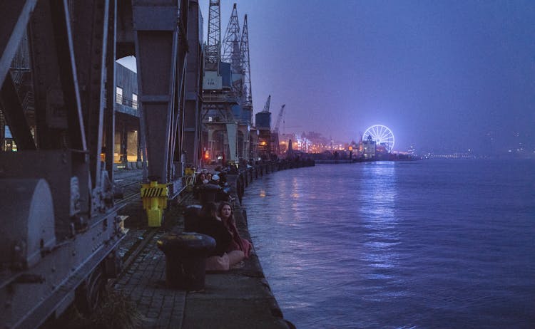 People Sitting On A Waterfront At Night