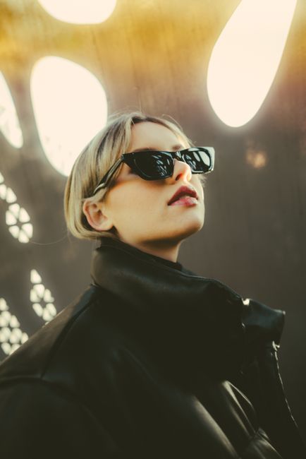 Close-up of a fashionable woman in sunglasses and coat, bathed in artistic lighting, showcasing modern style.