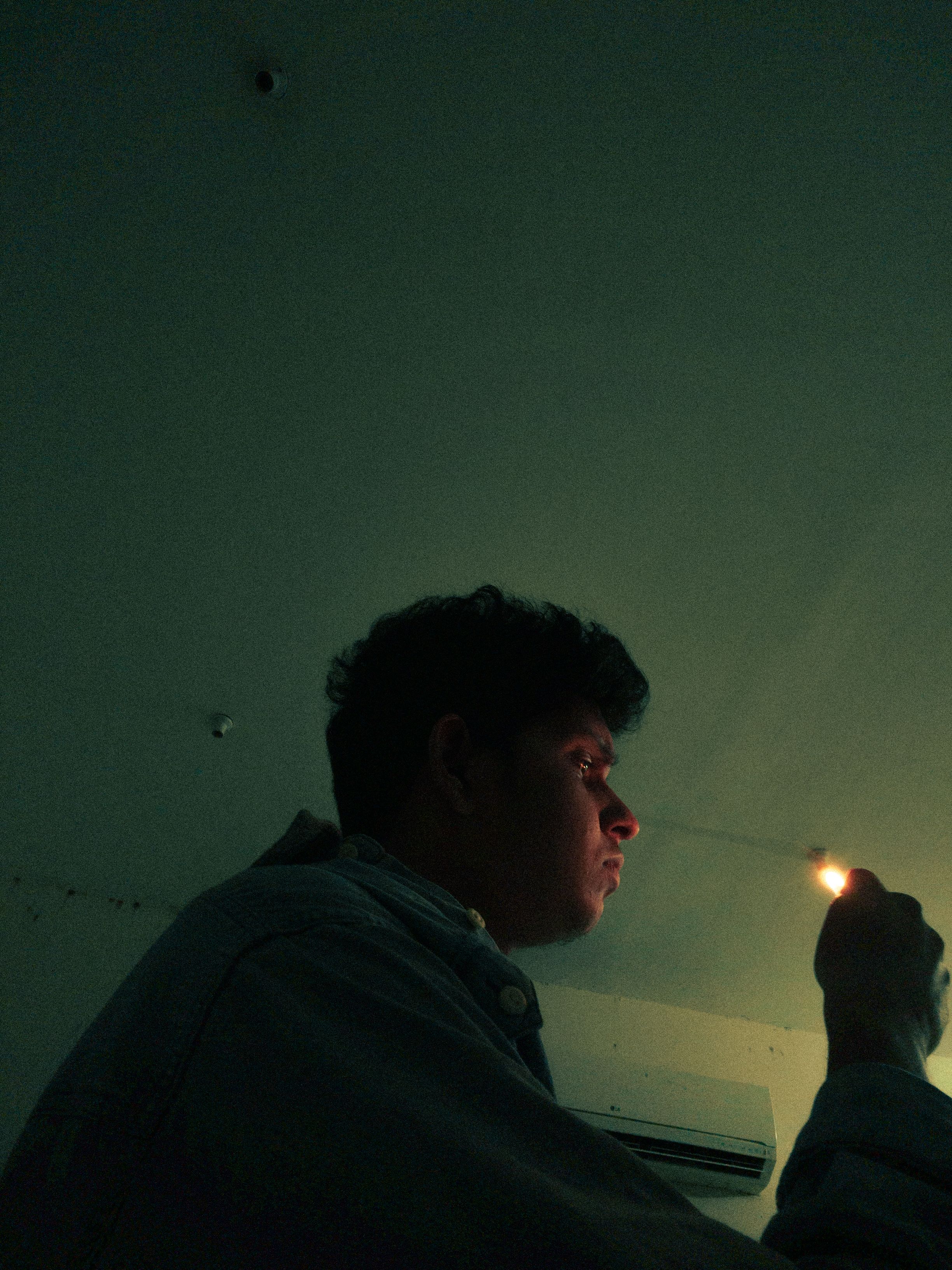 Side-profile of a man holding a lit lighter in a dimly lit room, creating a moody atmosphere.