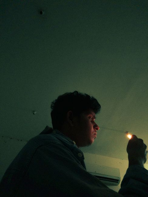 Side-profile of a man holding a lit lighter in a dimly lit room, creating a moody atmosphere.
