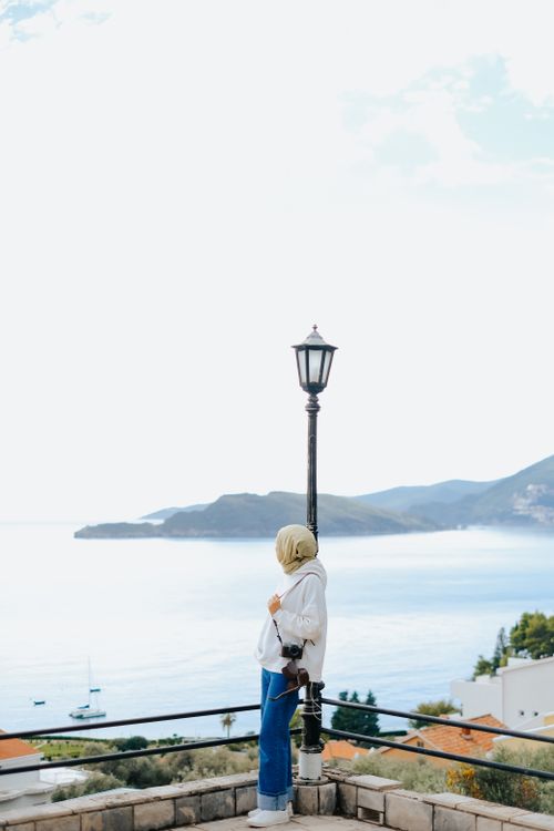 Free Woman standing by a lamp post overlooking a serene sea view. Stock Photo