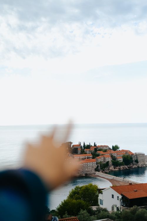 Free A blurred hand gestures towards a picturesque coastal village by the sea. Stock Photo