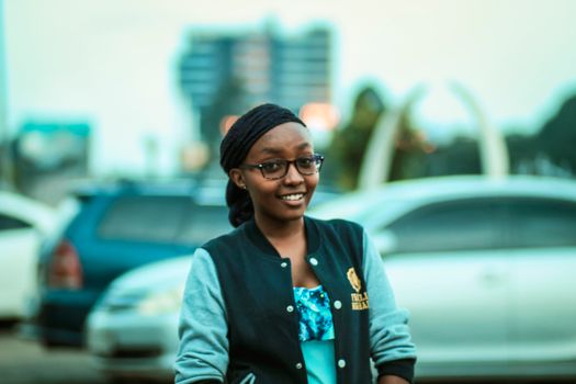 Smiling woman wearing glasses and a jacket outdoors in Nairobi, Kenya. Urban background.