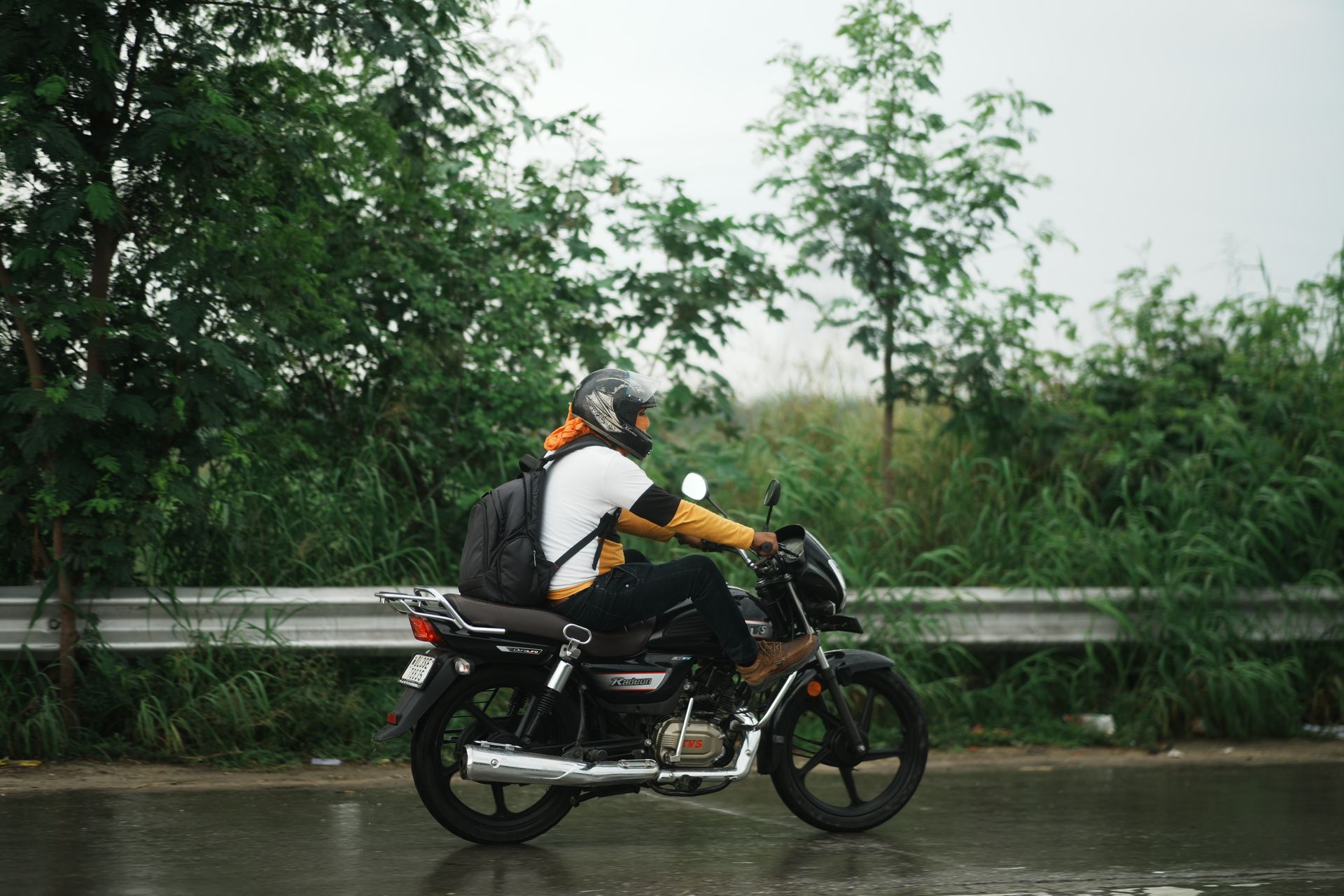 A person on a motorcycle rides along a wet road during a rainy day, showcasing outdoor transportation.