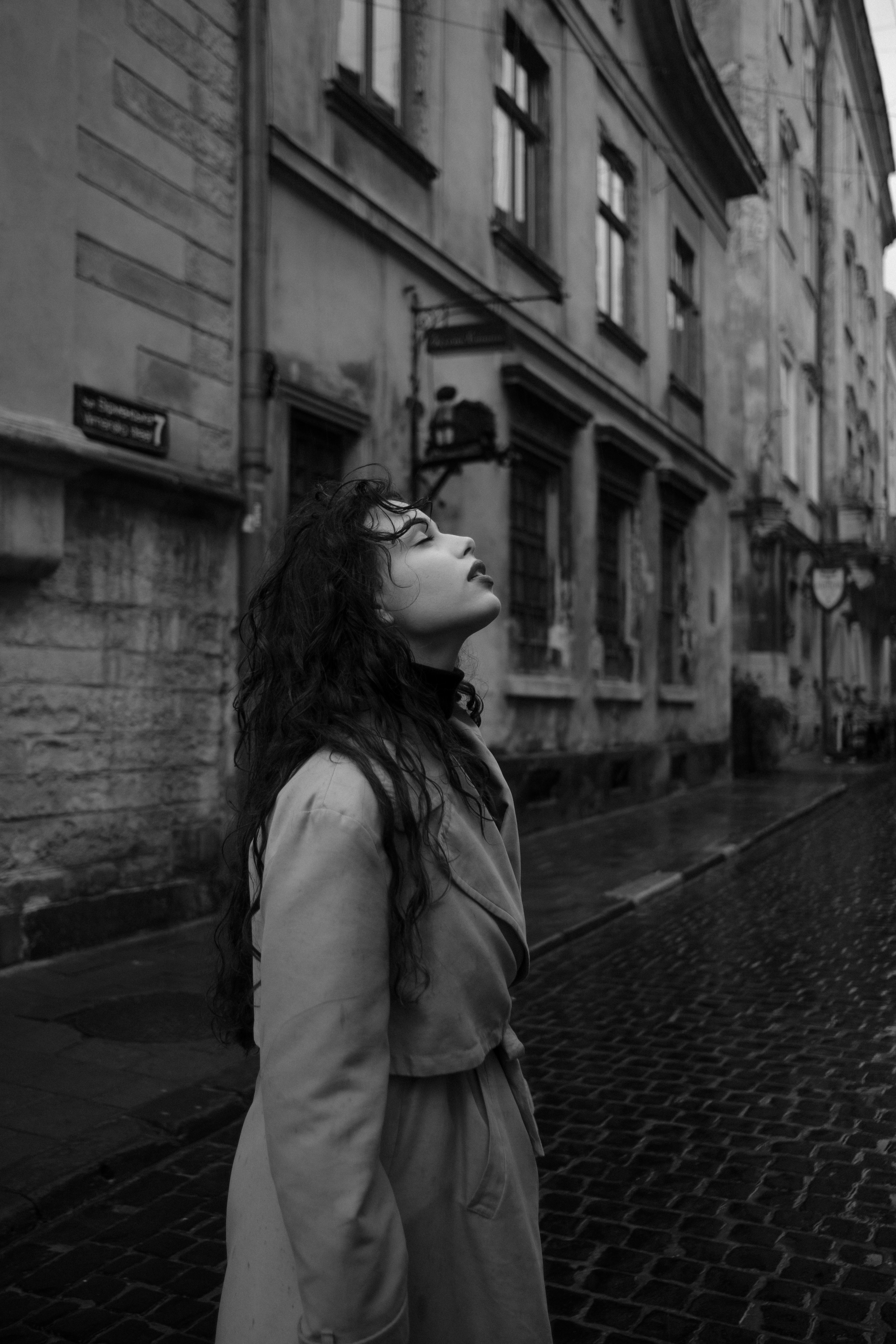 A woman looks upward while standing in a historic city street, capturing a contemplative mood.