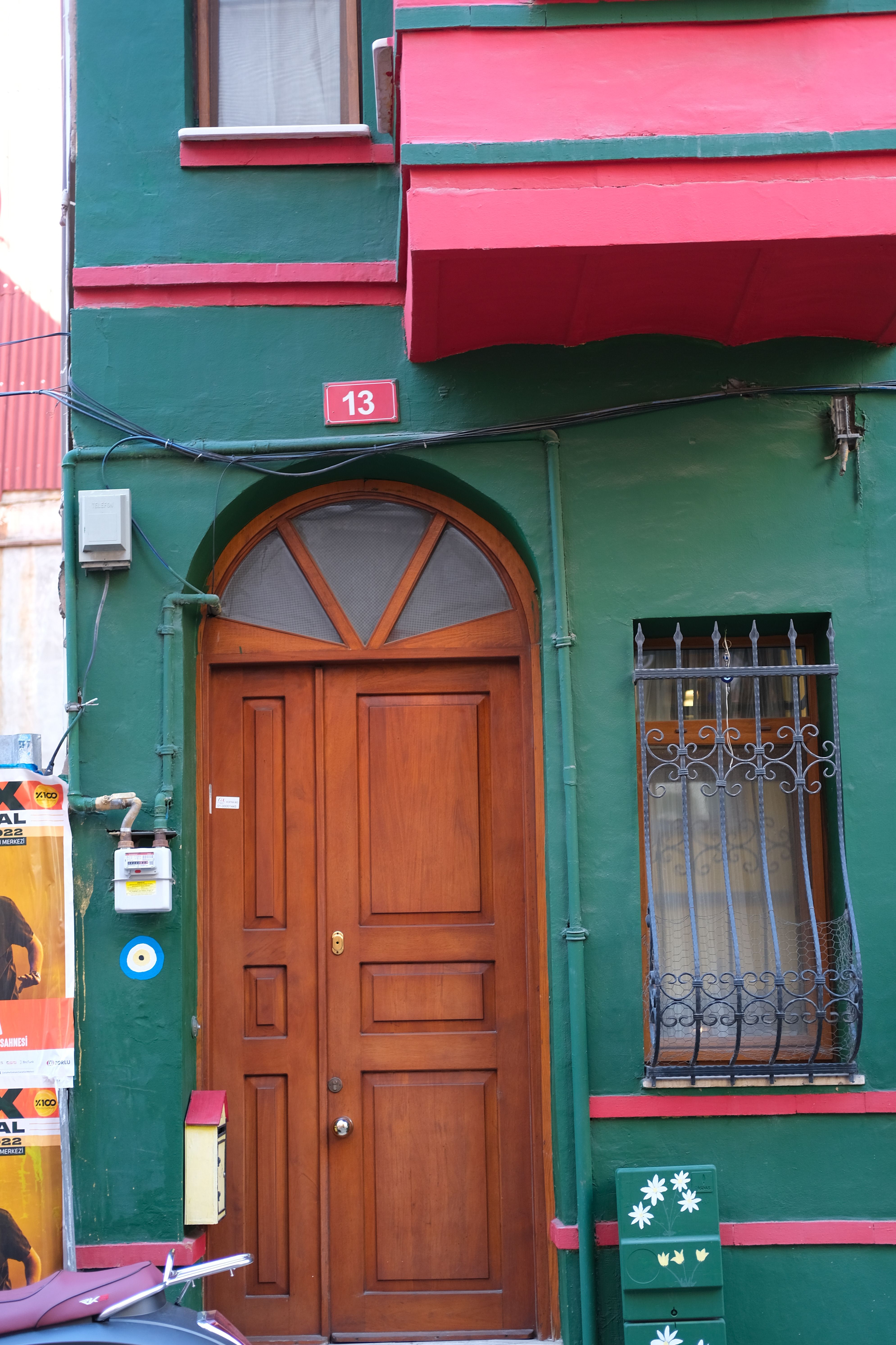 Colorful urban building exterior with wooden door, window grills, and vibrant green and red facade.