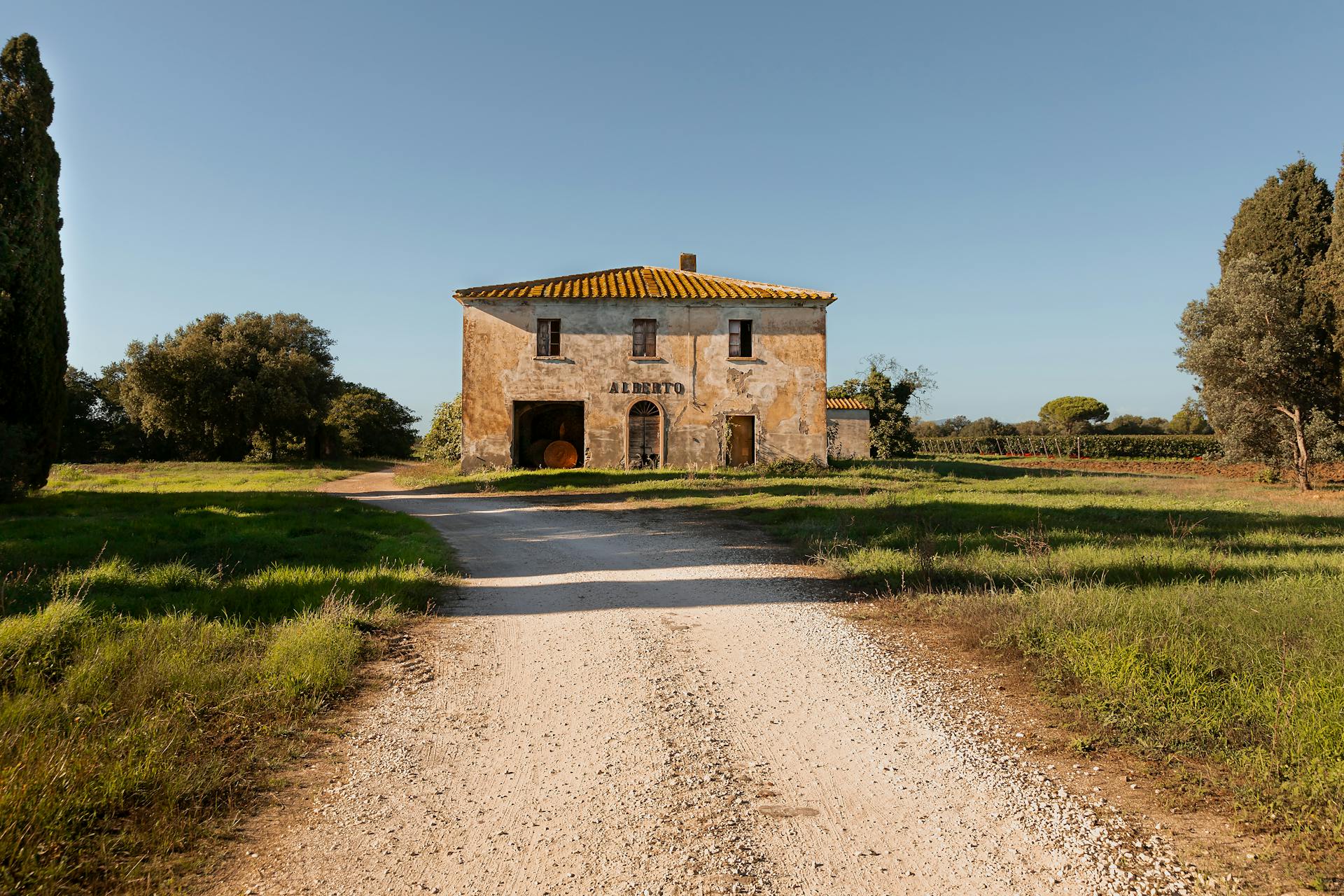 A picturesque rural Italian farmhouse stands at the end of an unpaved road, surrounded by nature.