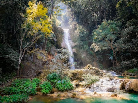 Serene waterfall cascading through dense jungle in Laos, surrounded by vibrant foliage.