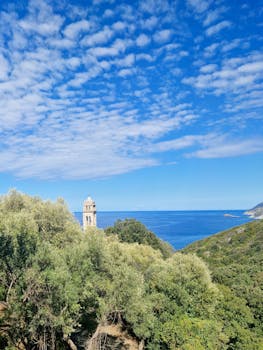 A beautiful coastal view of a historical tower in Corse, France with lush greenery and blue sky.