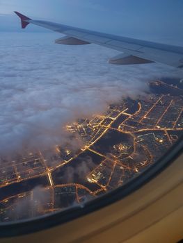 A stunning view from an airplane window of a city illuminated at night below the clouds.