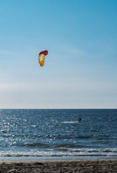 Kite surfer rides waves under clear blue sky, perfect for adventurous spirit.