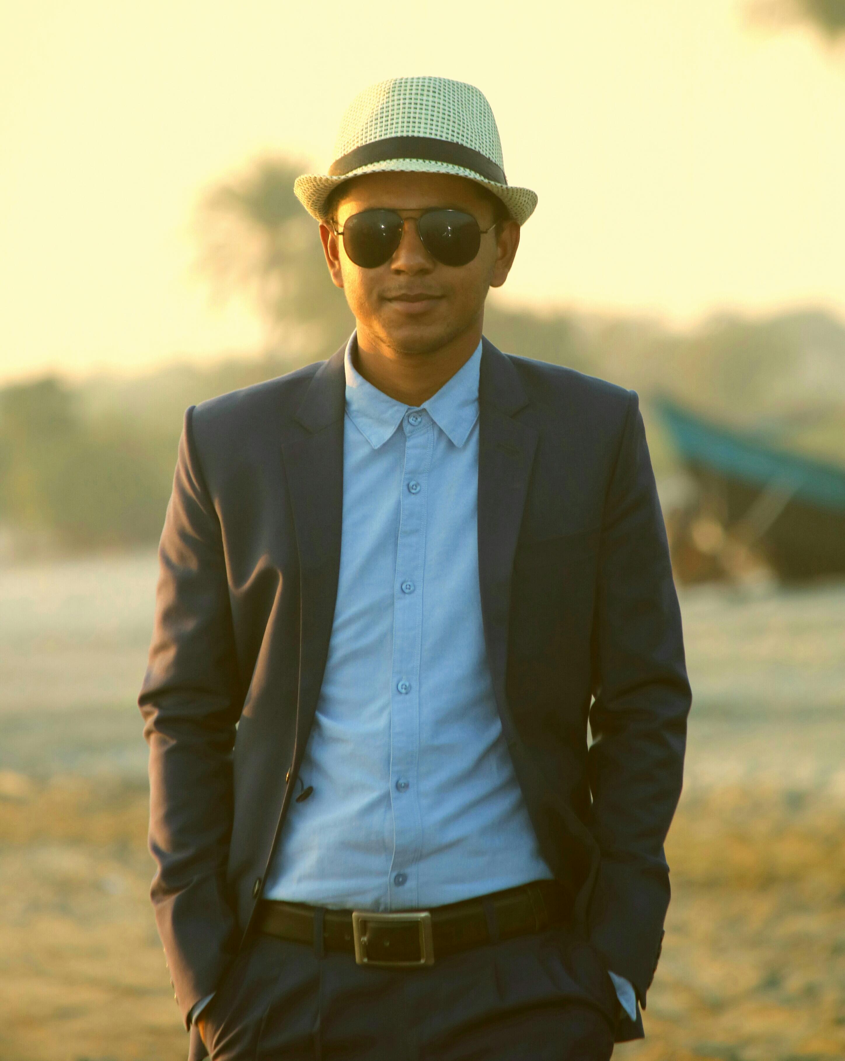 A fashionable man in a suit and hat poses confidently in Kuakata, Bangladesh, during the day.