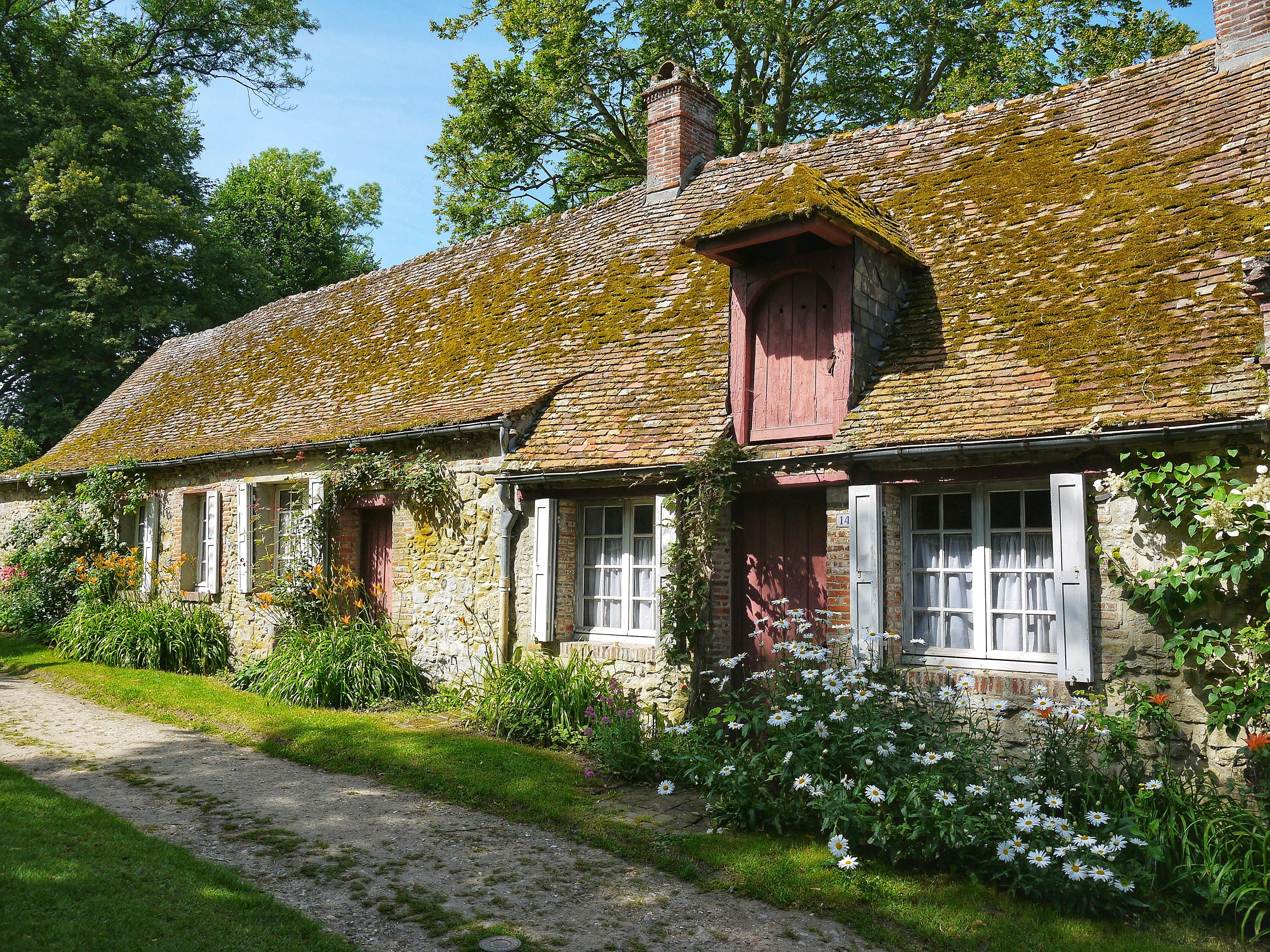 Idyllic stone cottage with mossy roof and vibrant garden in a peaceful setting.