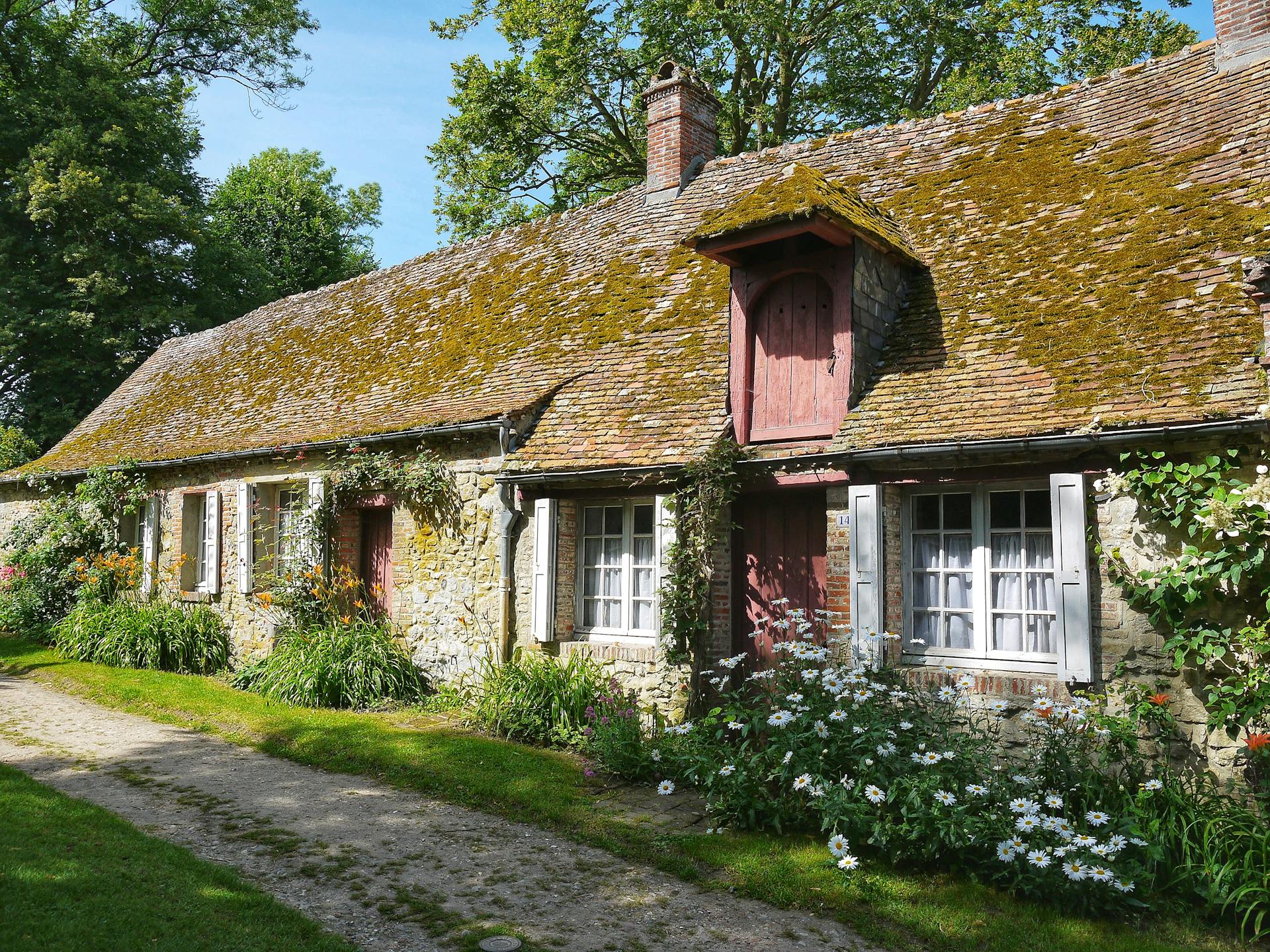 Idyllic stone cottage with mossy roof and vibrant garden in a peaceful setting.