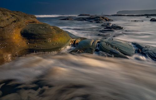 Free Capture of ocean waves flowing over rugged rocks in a dramatic seascape shot. Stock Photo