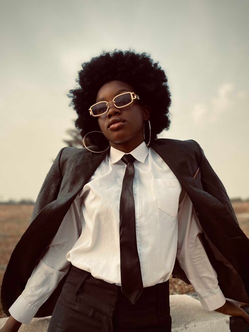 Free A fashionable woman poses confidently in a suit with sunglasses, capturing modern style and elegance. Stock Photo
