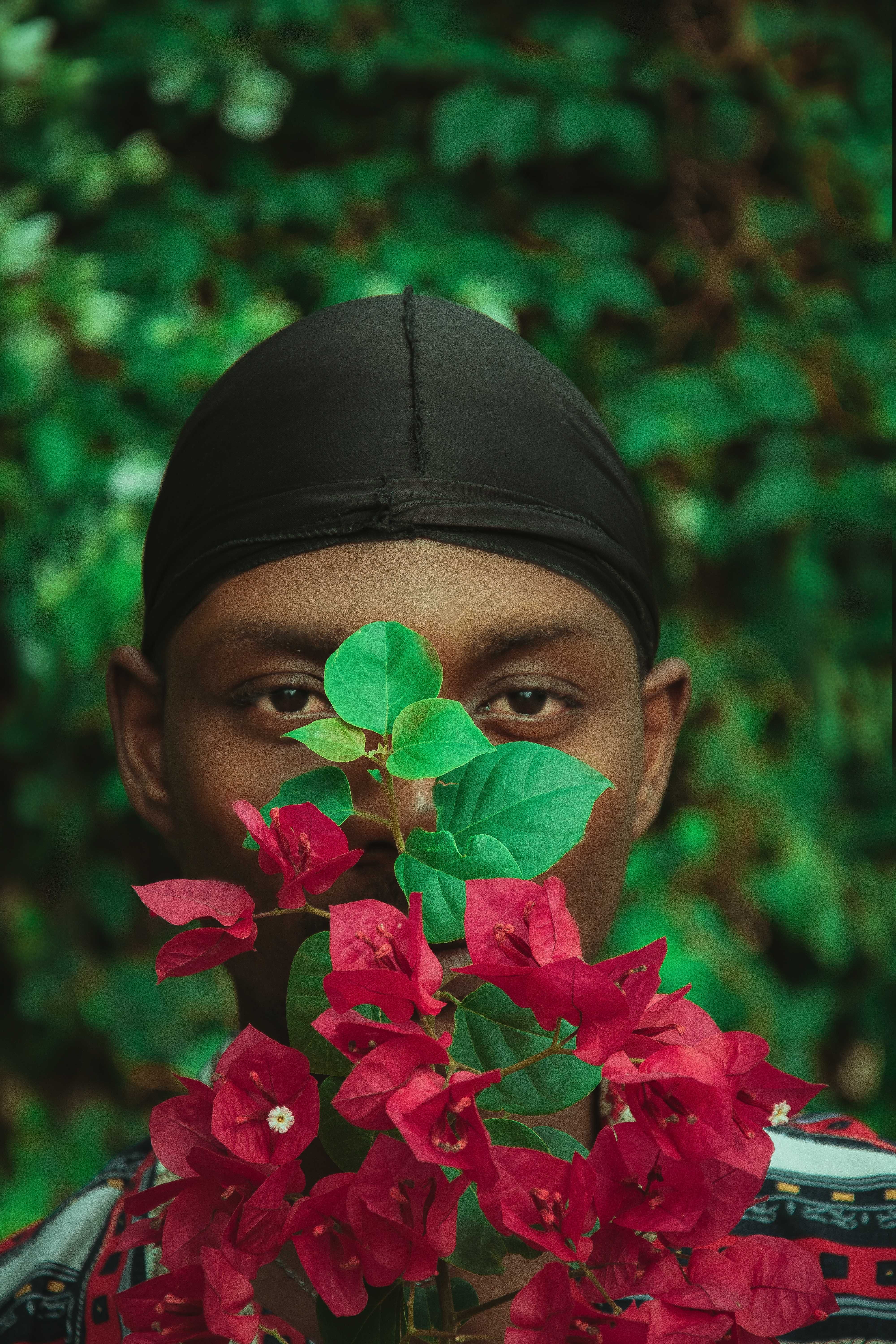 Man with red flowers in front of face against green garden background.