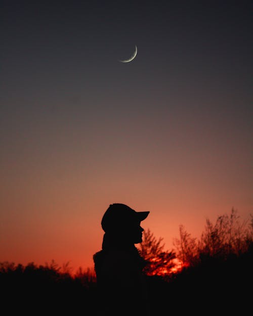 Silhouette of Person Wearing Cap under Crescent Moon